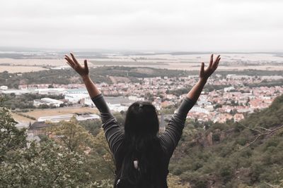 Rear view of woman with arms raised standing on mountain against sky