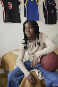 Contemplative female teenager with basketball sitting in bedroom