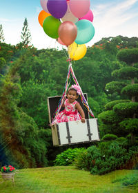 Portrait of cute girl in suitcase floating while tied to balloons