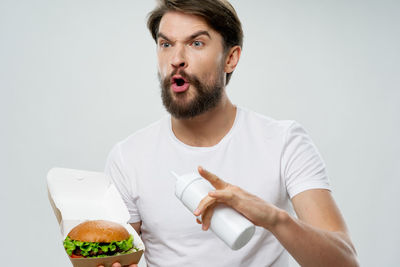 Portrait of young man holding food against white background