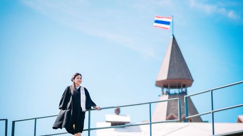 Portrait of smiling woman standing by building against blue sky