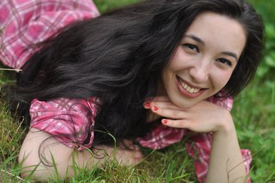 Close-up portrait of smiling young woman lying on grass