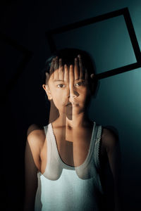 Portrait of boy covering face while standing against wall at home