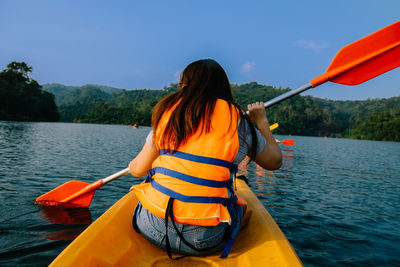 Rear view of woman kayaking on lake against sky