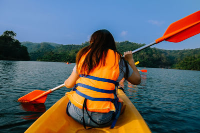 Rear view of woman sitting on boat against river