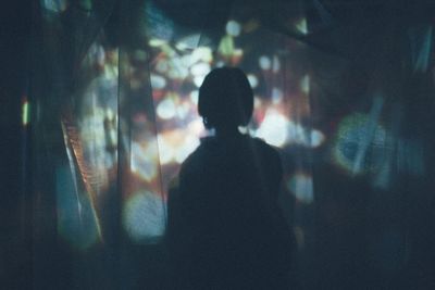 Rear view of silhouette woman seen through curtain at night