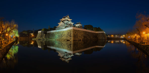 Reflection of illuminated buildings in lake against sky at night