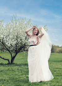 A young blonde in a long white dress poses near a cherry blossom in the garden, a spring landscape.