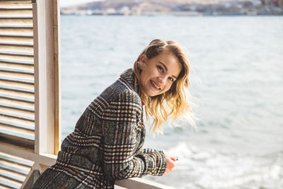 Portrait of smiling young woman by sea at window
