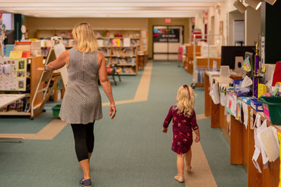 Rear view of mother and daughter walking in library