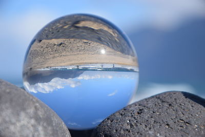 Close-up of glass on rock against blue sky