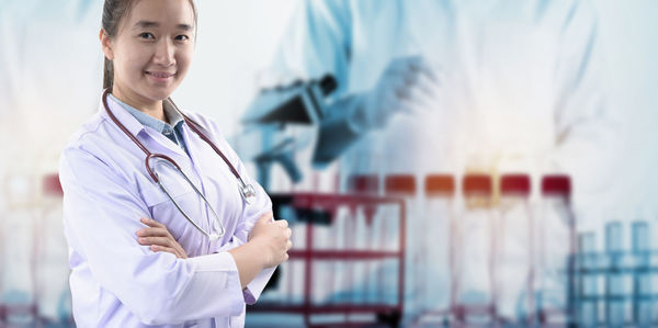 Digital composite image of smiling doctor with arms crossed standing against scientist