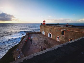 People on beach by lighthouse against sky