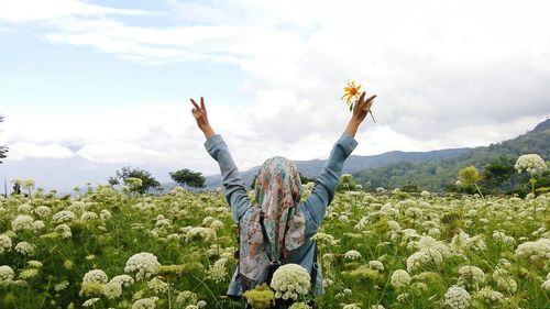 Woman with flowers on field against sky