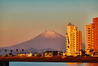 Buildings in city and snowcapped mountain during sunrise