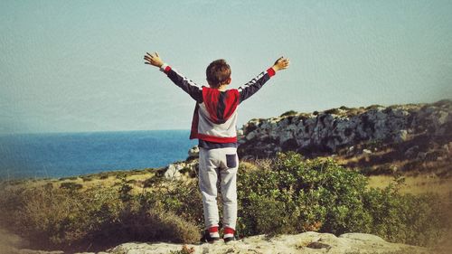 Man standing by arms outstretched against sky