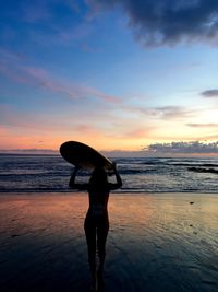 Silhouette woman standing at beach against sky during sunset