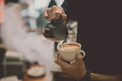 Midsection of man pouring milk in coffee at cafe