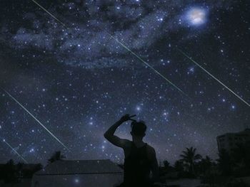 Rear view of man gesturing against starry sky at night