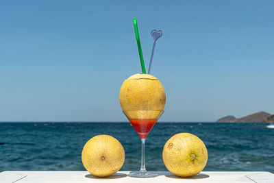 Glass of fruit on table by swimming pool against sea