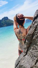 Rear view of woman with tattoo while standing by rock at sea