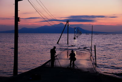 Rear view of silhouette people photographing on pier against sea during sunset