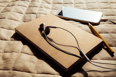 Close-up of in-ear headphones on book by mobile phone and pencil on sofa