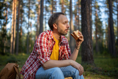 Rest in forest. carefree relaxed man taking break with healthy food eating sandwich while hike.