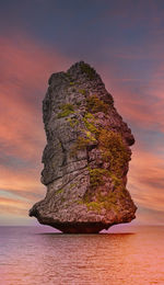 Rock formation in sea against sky during sunset