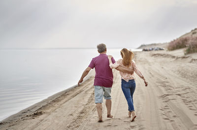 Father and daughter walking together on sand at sunset