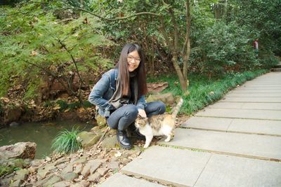 Portrait of happy woman crouching by stray cat on footpath at park