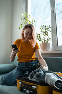 Young woman using mobile phone while sitting on sofa at home