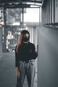 Woman wearing mask and sunglasses standing against wall