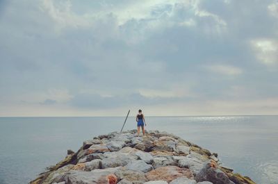 Rear view of man standing on sea shore against sky