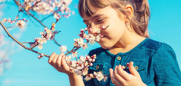 Happy girl with eye closed smelling flower under blue sky