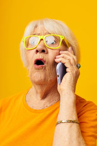 Close-up of young man using mobile phone against yellow background