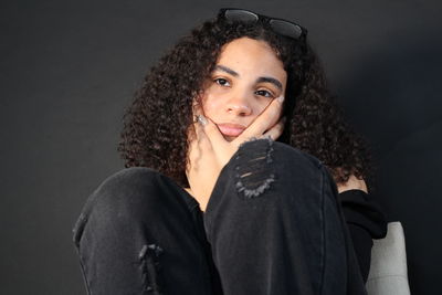 Portrait of young woman standing against black background