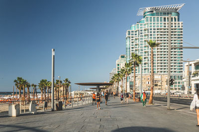 People on street by buildings against clear blue sky