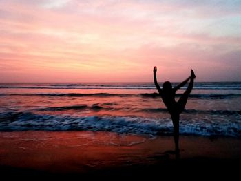 Silhouette person exercising at beach against sky during sunset