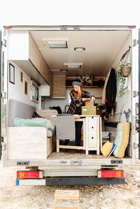 Traveling female hipster standing in parked truck and packing various stuff during trip in summer