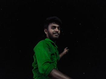 Portrait of young man standing against black background