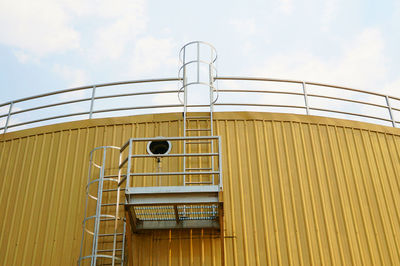 Low angle view of yellow cylindrical tank against sky