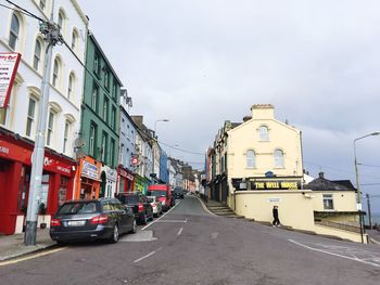 Cars on road by buildings in city against sky