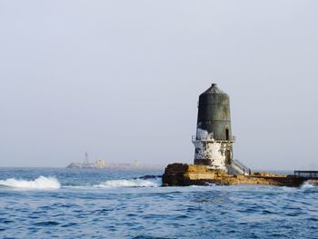 Lighthouse by sea against clear sky
