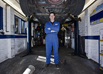 Car mechanic posing under a car at automotive garage in the uk