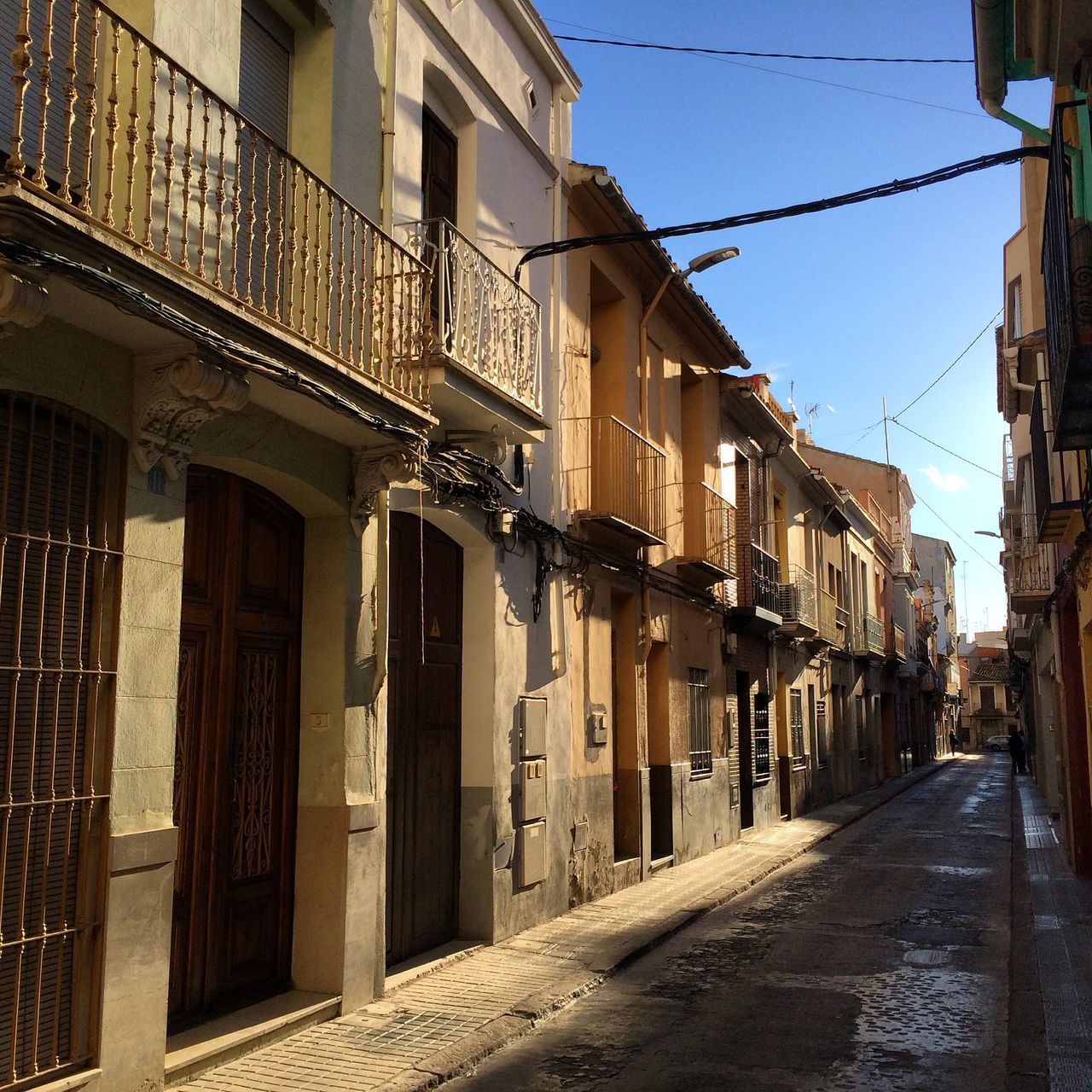 architecture, building exterior, built structure, street, the way forward, residential building, residential structure, power line, city, clear sky, building, diminishing perspective, sky, house, town, road, cable, cobblestone, outdoors, old town