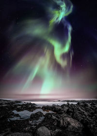 Aurora borealis over snowcapped mountains against sky