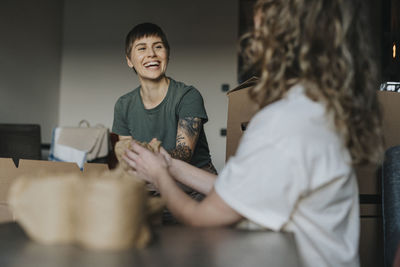 Happy lesbian woman sitting with girlfriend and wrapping stuff during relocation