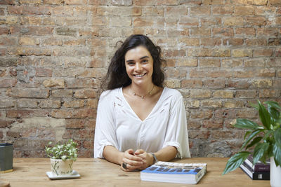 Portrait of young woman using mobile phone while standing against brick wall