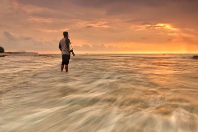 Rear view of man on beach against sky during sunset